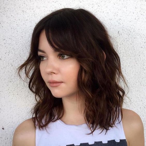 A dark brunette long bob with caramel balayage, curtain bangs, and waves is a stunning solution to try