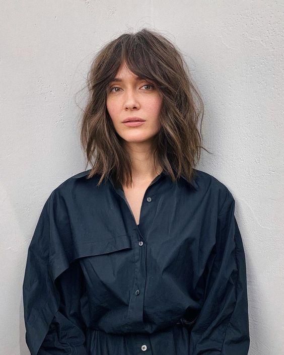 A long brown bob with slight highlights, messy waves, and bottleneck bangs, a trendy solution to rock now