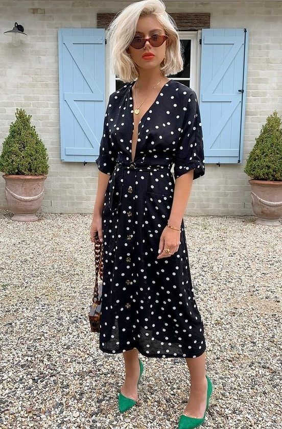 Black polka dot midi dress featuring a plunging neckline, paired with a chic bag adorned with a chain and bold green shoes, a great idea for a summer date