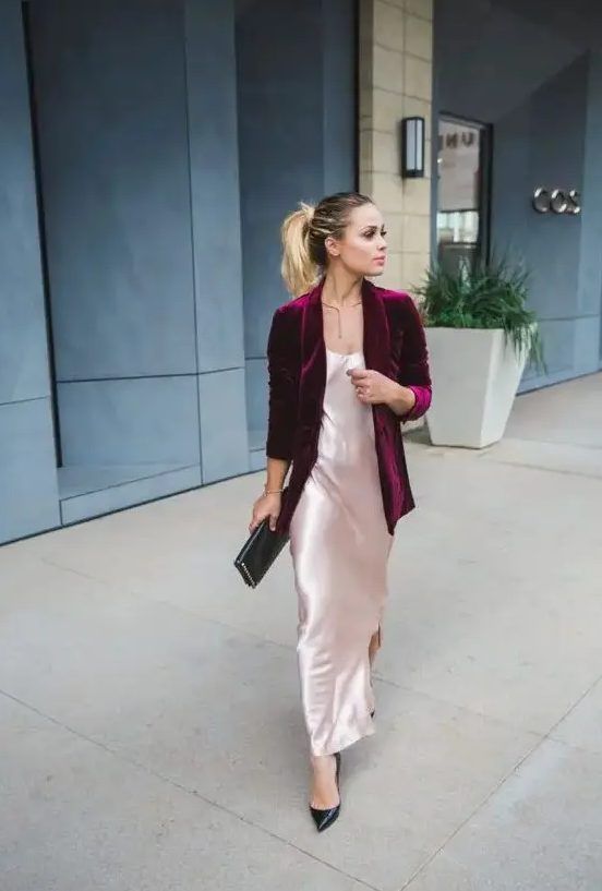 Blush slip maxi dress, complemented by a purple velvet blazer, black pumps, a black clutch, and a statement necklace