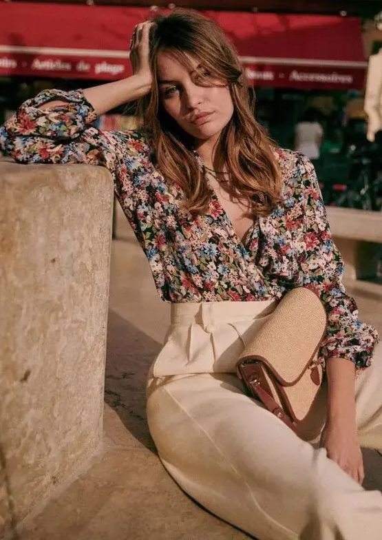 Bold floral wrap blouse with short sleeves, creamy high-waisted pants, and a small bag, a cool combo for a casual summer wedding