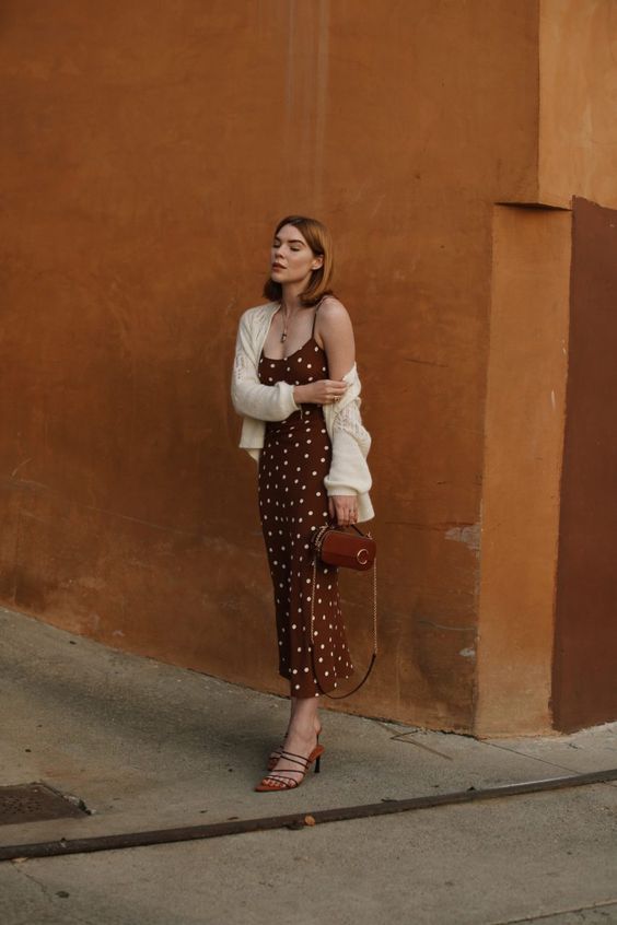 Brown polka dot slip dress, white cardigan, strappy mules, and a small brown bag for a chic look