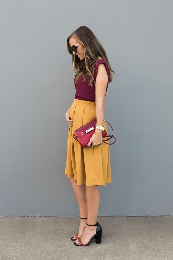 Burgundy top with no sleeves, marigold knee-pleated skirt, a burgundy clutch, and two-tone block heels