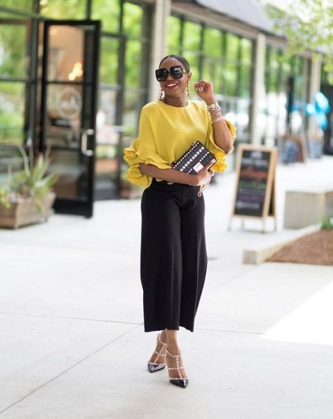 Casual outfit with black culottes, a sunny yellow top with ruffled sleeves, black spike shoes, and a black clutch