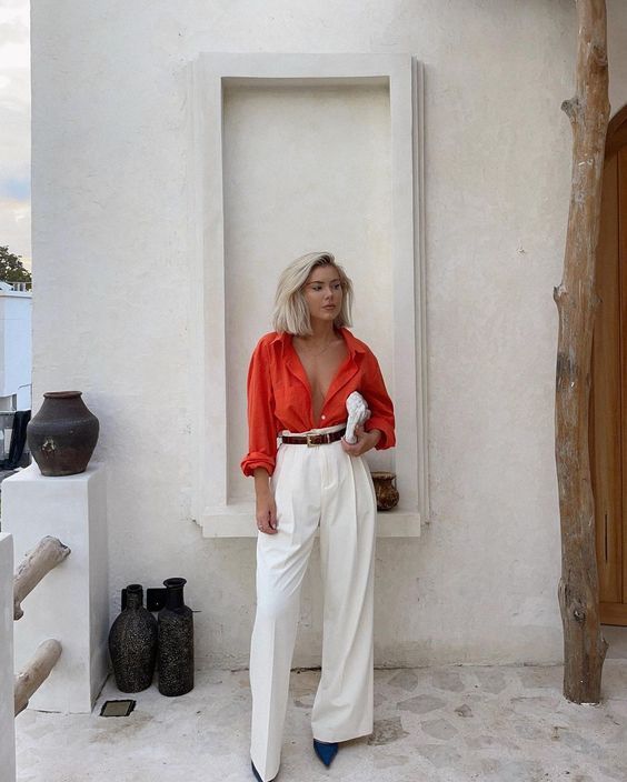Casual summer wedding guest look with an orange shirt, white pants, black shoes, a brown belt, and a white bag