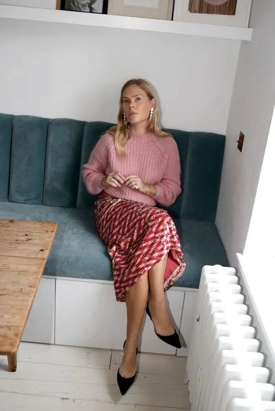 Cozy wedding guest outfit with a pink chunky knit sweater, red printed sequin skirt, black shoes, and pearl earrings