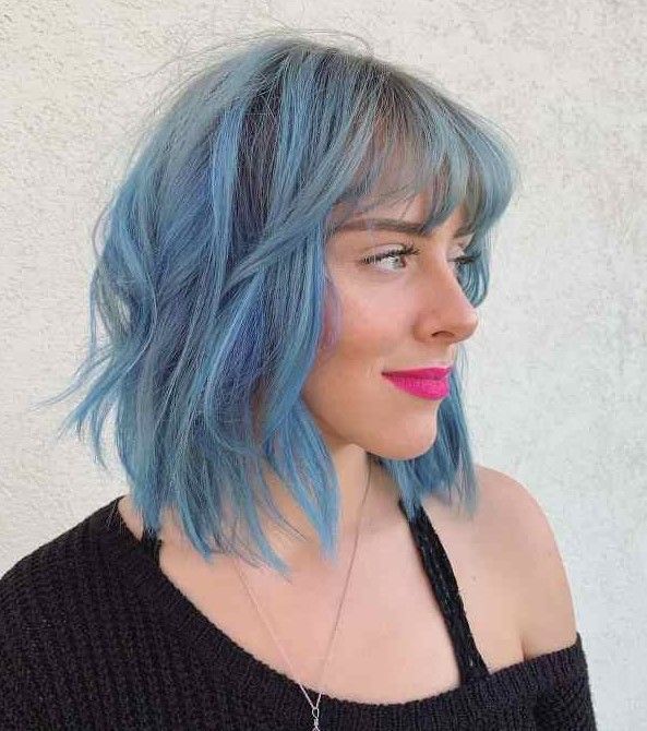 Edgy shaggy long bob with bangs done in light blue with waves that bring texture and movement to the look