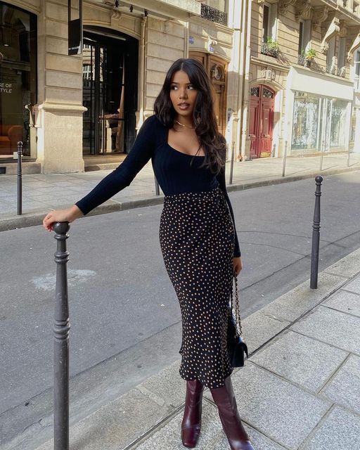 Fitted black top with square neckline, paired with a black midi polka dot skirt, burgundy boots, and a black bag for a stylish appearance