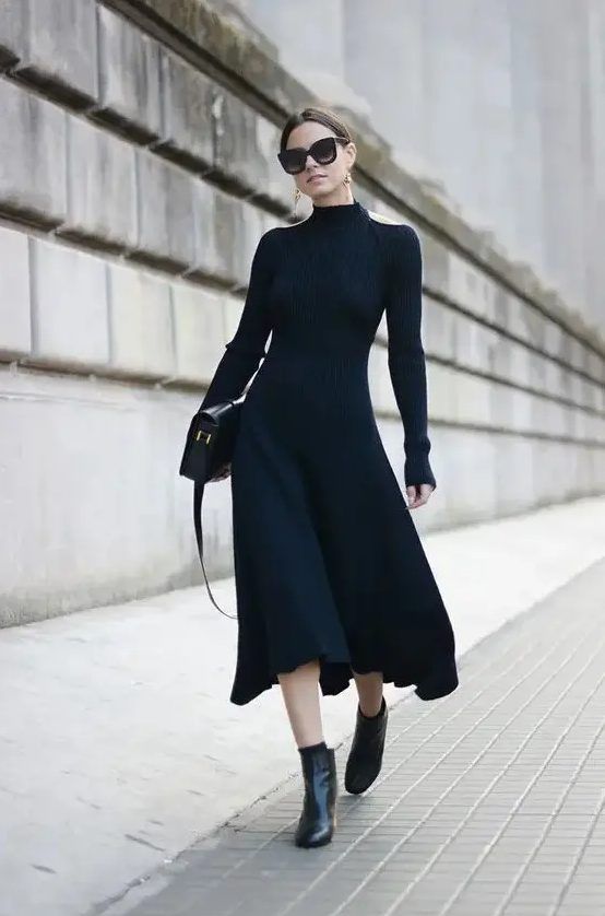 Gorgeous black fitting midi dress with cutout shoulders and long sleeves, black boots, statement earrings, and a black bag