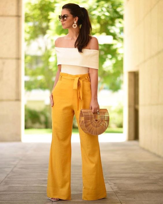 High-waisted yellow pants, a creamy off-the-shoulder top, a straw bag, and statement earrings