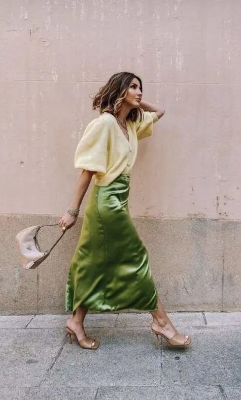Lovely fall wedding guest look with a neutral cardigan tucked into a green satin midi, tan mules, and a tan bag