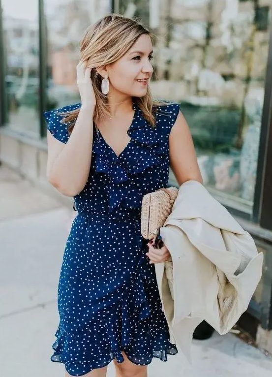 Navy and white polka dot mini dress with ruffles, no sleeves, V-neckline, white jacket, and a wicker clutch