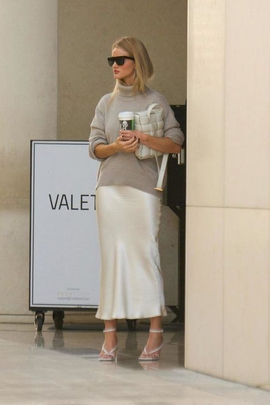 Rosie Huntington Whiteley donning a grey turtleneck jumper, a white midi slip skirt, white strappy shoes, and a white bag