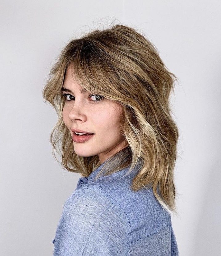 Wavy blonde long bob with layers and curtain bangs, giving a 70s vibe to the look