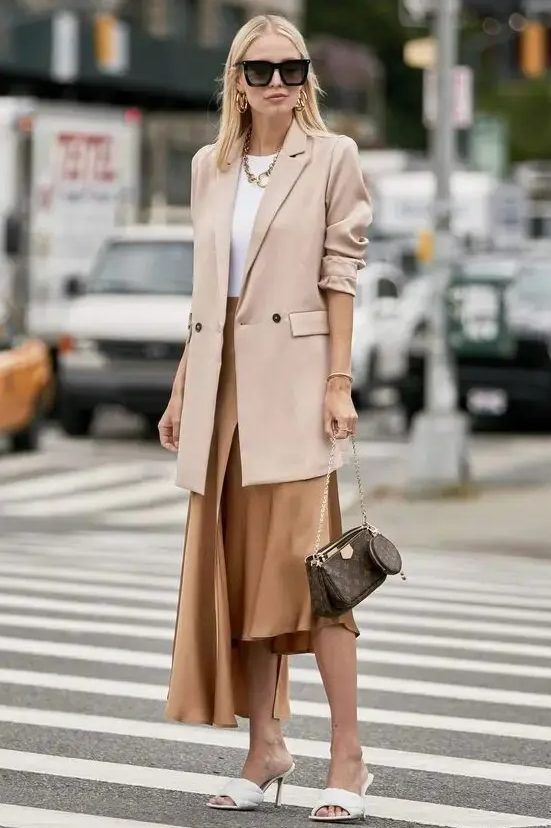 White top, chic asymmetrical skirt, white mules, blush oversized blazer, statement accessories, and a brown bag